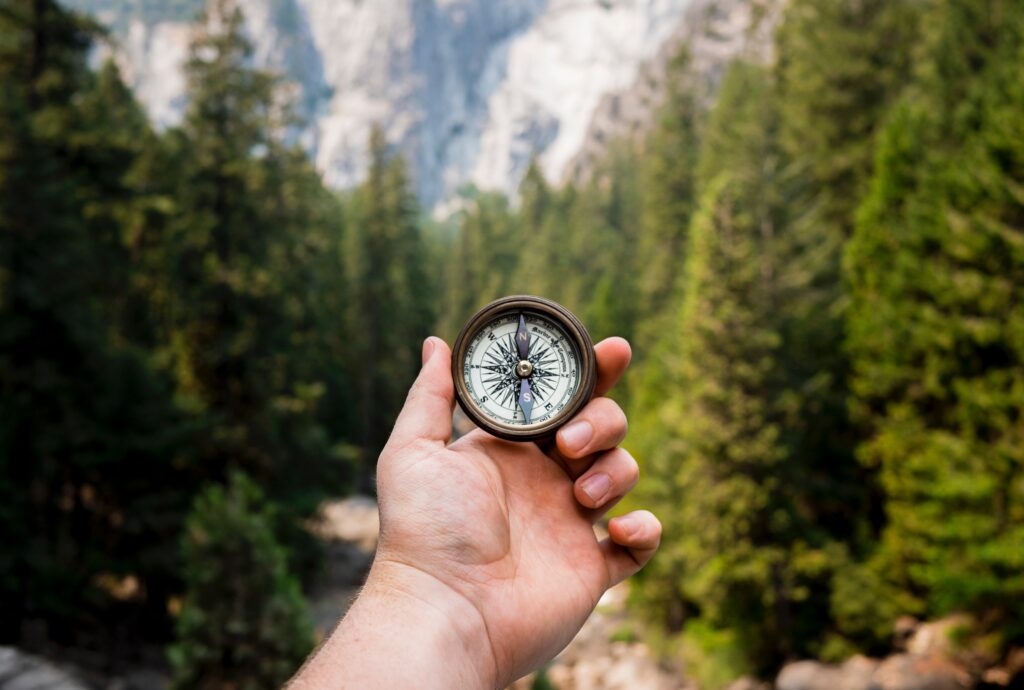 Hand mit Kompass vor Berglandschaft – Symbol für Orientierung und Steuerung im Projektmanagement